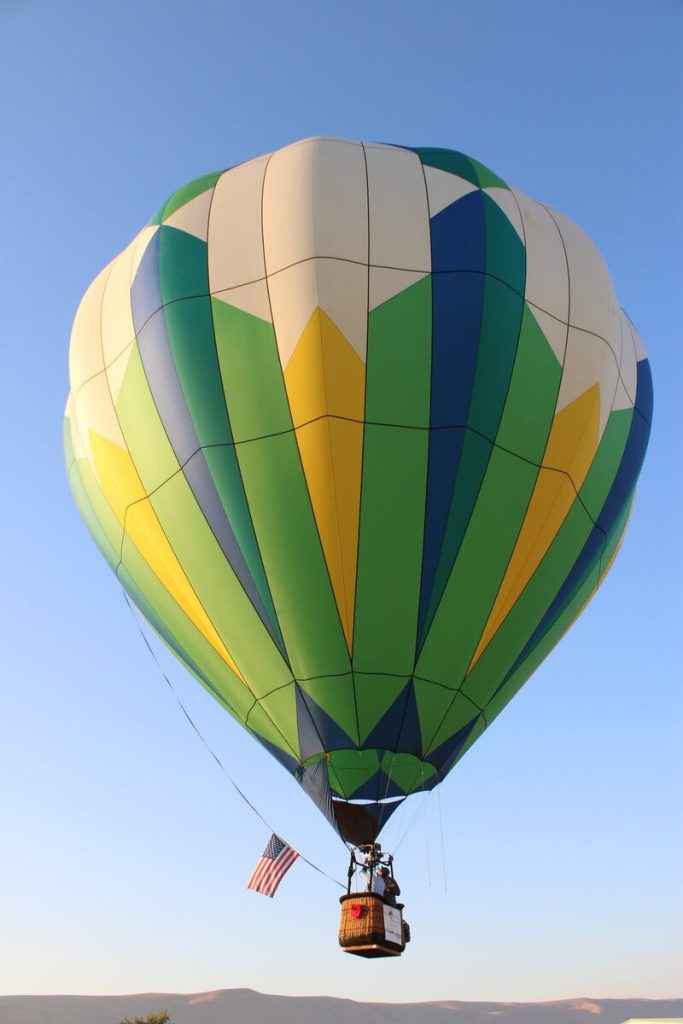 Green and yellow balloon floating in a blue sky