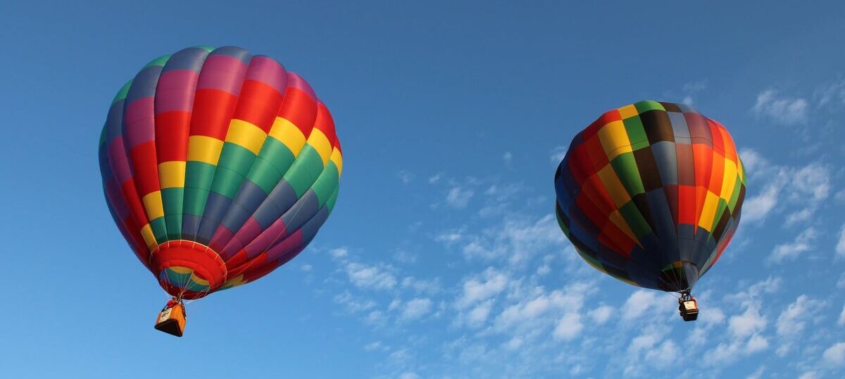 Two hot air balloons floating in an open blue sky