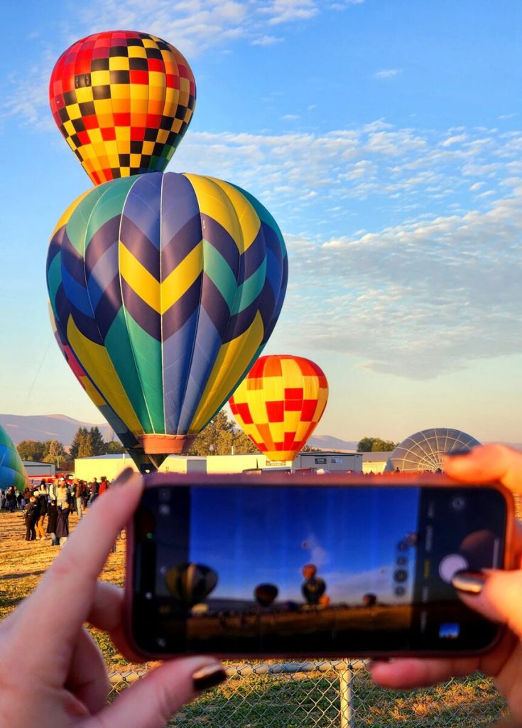 Spectator photographing colorful balloons at launch